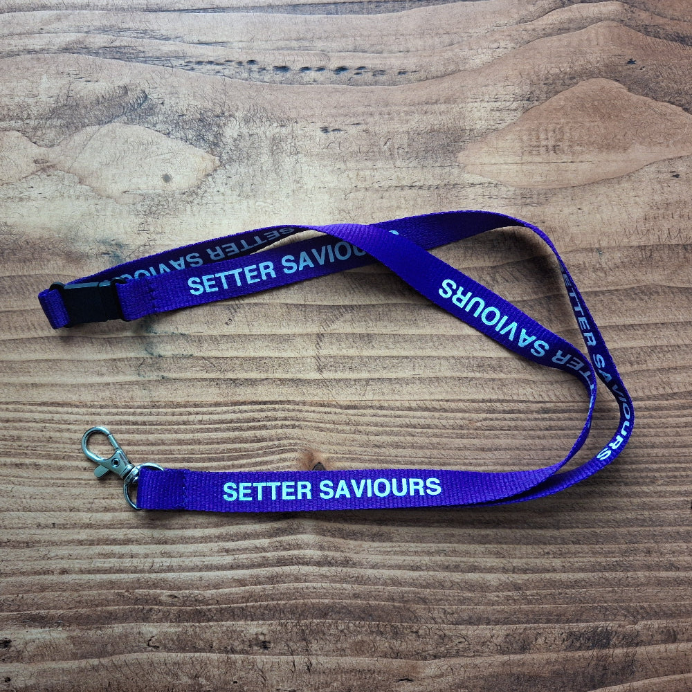 A purple lanyard with white text reading 'SETTER SAVOURS' laid out on a wooden surface, featuring a silver metal clasp and a black plastic connector.